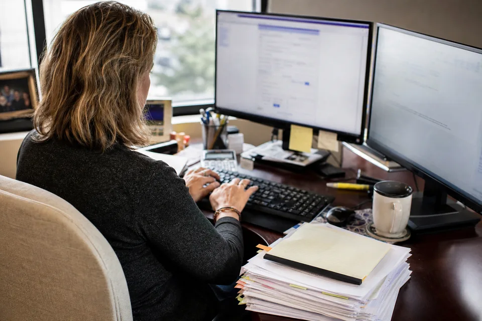 Paralegal at an estate planning firm building a document template next to a stack of printed will and trust drafts