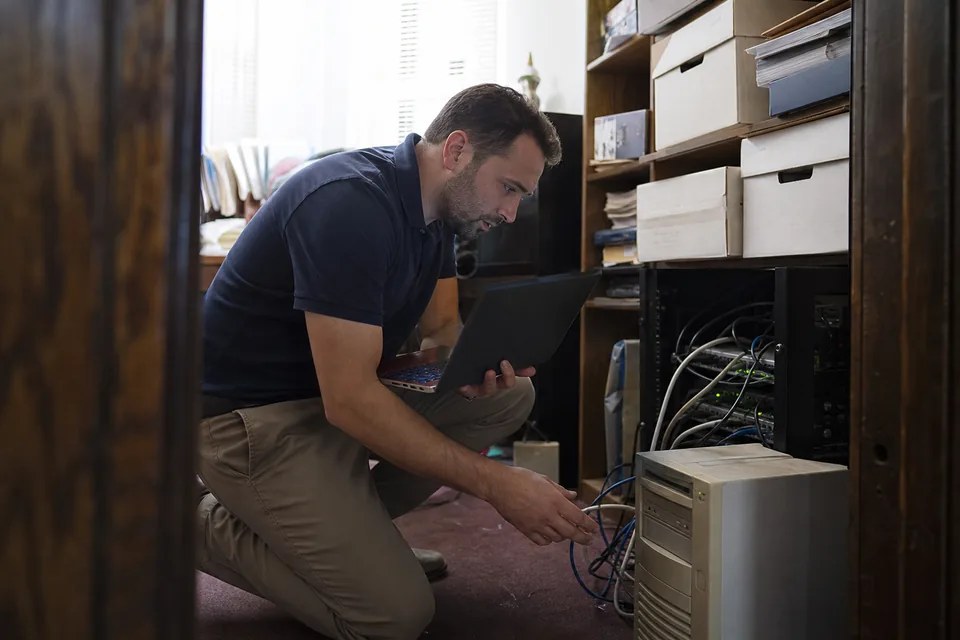 Office manager at a small law firm next to an aging desktop tower and server closet while a laptop shows a cloud billing login screen